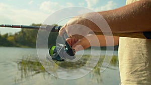 Close-up of fisherman holding fishing rod and turning reel during angling