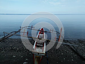 Close up of fishing boat on black sandy beach with calm sea water and blue sky early in the morning