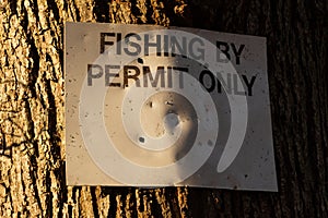 Close up of a fishing by permit only sign attached to a large tree in the winter