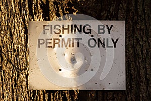 Close up of a fishing by permit only sign attached to a large tree in the winter