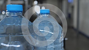 Close-up of five-liter bottles traveling on a conveyor belt from the camera. Production of drinking water at a food processing pla