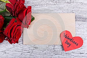 Close-up of five red roses on a gray background, with a paper heart and an envelope, the day of the holy Valentine.