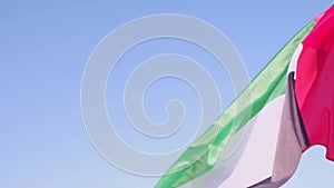 Close-up of the flag of the United Arab Emirates waving in the wind against a cloudless blue sky.