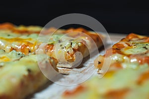 Close up flat bread pizza by cheese on a cutting board with flour in black background.