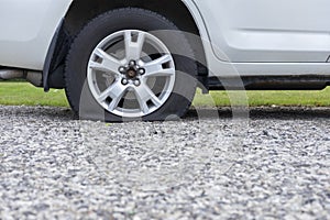 Close up of flat rear tire of white suv track car vehicle automobile punctured by nail. Summer day, residential street.