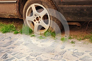 A close-up on a flat tire of an old car on a pebbled road side covered with grass