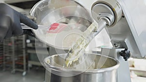 Close-up of flour adding to raw dough in automatic mixer. Female hand in black gloves pouring ingredient in metal bowl