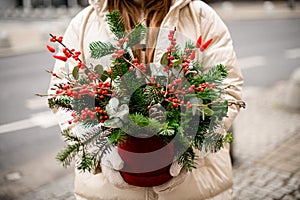 Close-up of flower arrangement in pot of spruce branches and red berries and eucalyptus in female hands