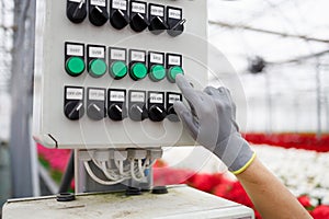 Close-up of a flower greenhouse worker`s hand in a glove pressing a button on the control panel