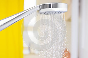 Close-up of flowing water drops from a shower head in a bright bathroom