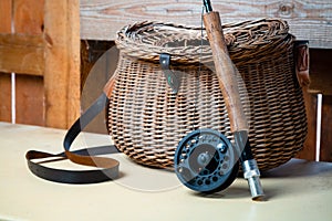 Close up of fly fishing rod with reel next to braided basket. Fly fishing equipment still life. Nobody