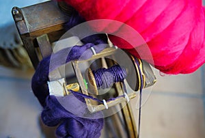 Close up of flyer with red and blue raw merino wool from old wooden spinning wheel