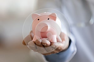 Close up focus on piggy bank in doctor hands.