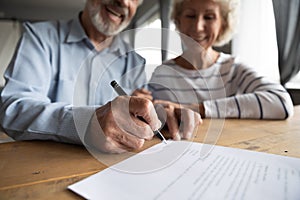 Close up focus on wrinkled male hand signing paper document.