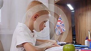 Close-up of a focused schoolboy boy reading an book at home at his desk.