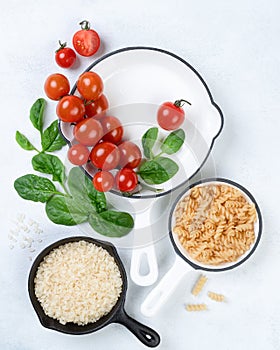 Close up Food background with vine tomatoes, spinach leaves, white rice, fusilli pasta and cast iron skillet. Top view, copy space