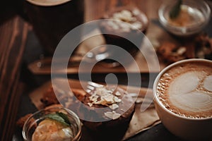 Close up food image of cup of coffee and dessert on the wooden table background in cafe. Trend warm toning. Photo with a small dep