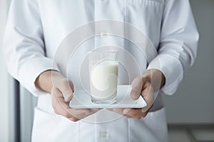 Close-up of a food inspector\'s hands holding a glass of milk on a tray, against a clinical background