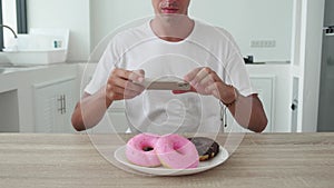 Close up - Food photographer take pictures with smartphone of colored fresh donuts in plate on kitchen background