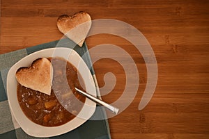 Close up food photography with overhead view of hot homemade chicken soup with love heart shape toast on wood for Valentines Day