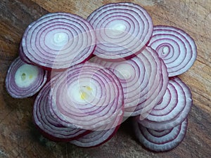 Thin slices of red onions on wooden chopping board