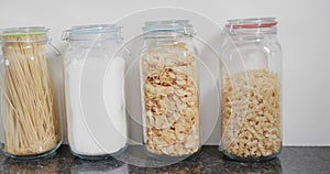 Close up of food storage jars with flour and various kinds of pasta on shelf in kitchen, slow motion