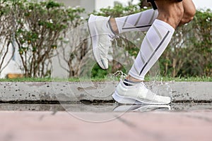 Close up on foot with freeze action of athlete`s legs and running shoes splashing water after heavy rain