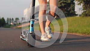 Close-up foot or leg of young woman walking on sidewalk with blue scooter. Girl walking in park on sunset. Teenager