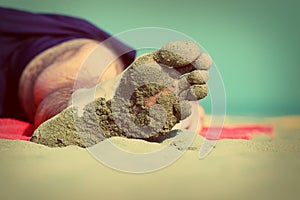 Close-up of the foot of a sleeping man lying on the beach