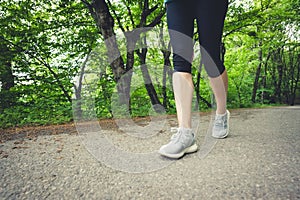 Close-up of a foot of a sporty girl in leggings and sneakers before jogging in the forest. The concept of outdoor sports