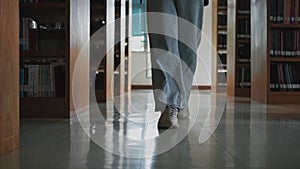 Close-up foot of student girl walking between shelves in library