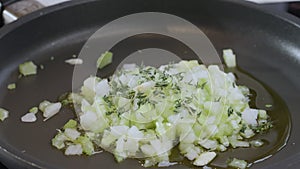 Close-up footage of chopped white onions frying in a pan in hot olive oil. The cook adds rosemary. Slow motion footage.