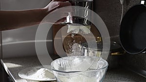 Close up footage of hand sifting white flour into glass bowl with a steel sieve.