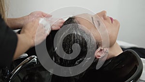 Close up footage of washing head of woman with long, dark hair with shampoo. Massaging the head sculp. Close up hands of