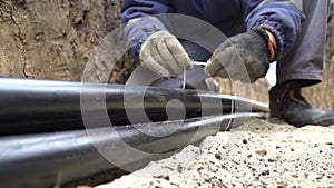 Close up footage of a worker using zip ties on three thick cables in a trench