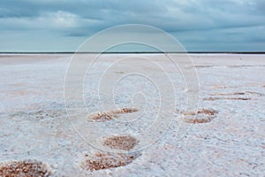 Close-up footsteps on salt pink lake, cloudy sky