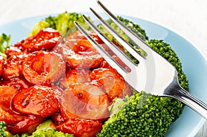 Close up of fork on plate with broccoli and slices of sausages