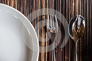 Close-up fork with spoon and white dish on wooden tablemat