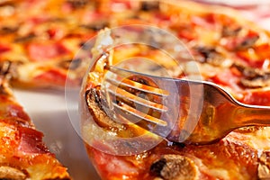 Close up fork takes a piece. Pizza with ham and mushrooms. Delicious hot food sliced and served on white platter. Menu