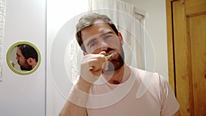 close up fornt view of a young man brushing teeth looking at camera, handsome guy enjoying morning oral hygienic routine, beauty