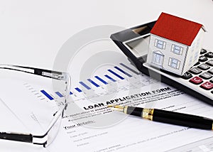 close up of fountain pen and loan application form and paper house on calculator and eyeglasses for Home loans concept
