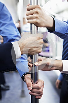 Close-up of four business people's hands holding the pole on the subway