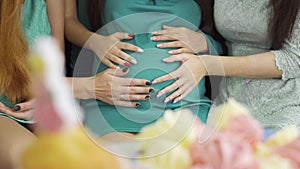 Close-up of four female caucasian hands caressing belly of the expectant woman. Young women having pre-bith party and