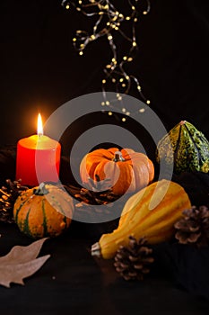 Close-up of four green and orange pumpkins, with autumn leaves and burning orange candle, selective focus, on dark wooden table