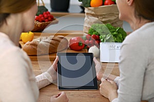 Close-up of four human hands are gesticulate over a tablet in the kitchen. Friends having fun while choosing menu or