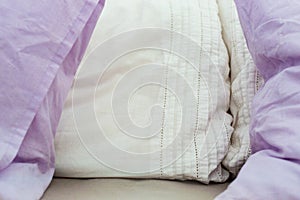 Close up of four white and lilac pillows on messy bed