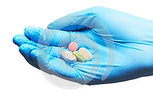 Close up of four white, pink and green tablets on female doctor's hand in blue sterilized surgical glove