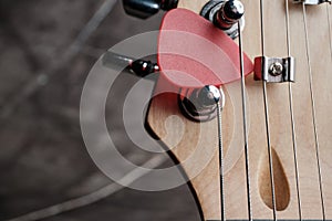 Close-up of a fragment of a guitar neck and a red plectrum on a dark background. Selective focus