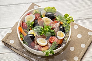 Close up. French cuisine. Traditional niÃ§oise nicoise salad in a white plate on a polka dot napkin. White background