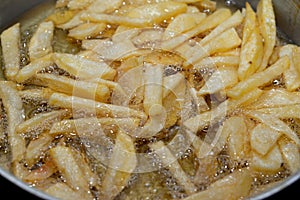 Close-up of French fries potatoes frying in boiling hot oil in a deep fryer at home. French fries, Junk food concept, home made